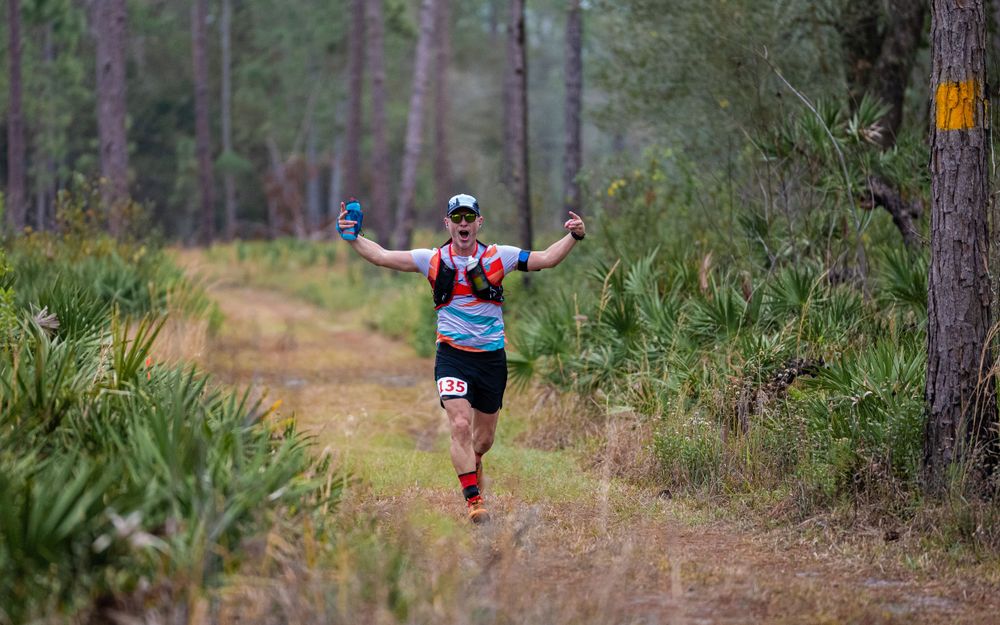 Trail runner celebrates with arms outstretched on a scenic forest path.