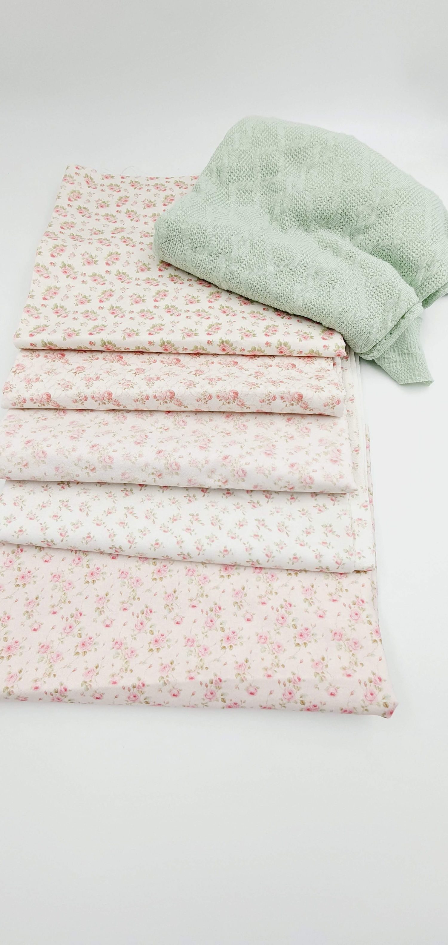 Stack of vintage floral print fabrics in soft pink and white with a mint green pillow on top.