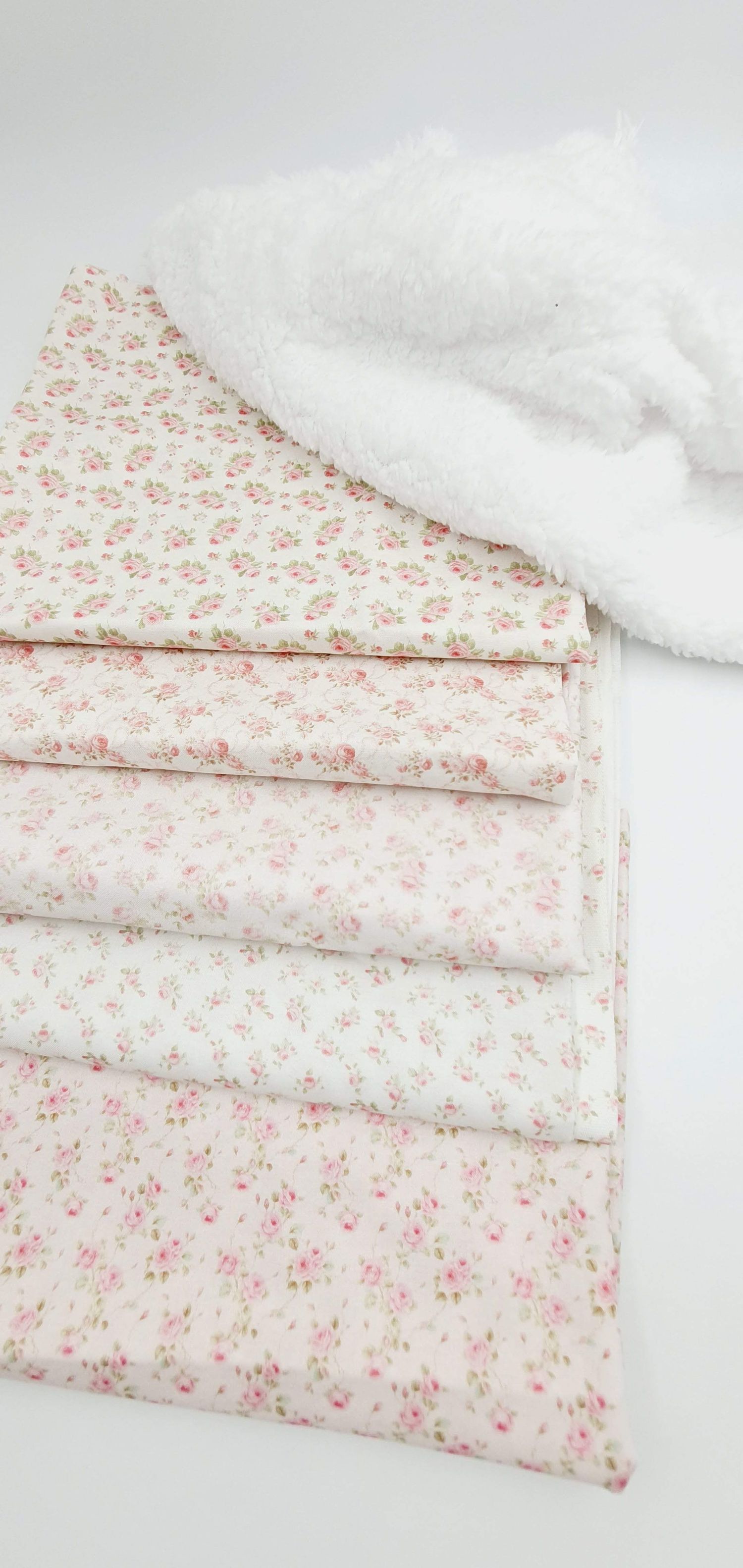 Folded white cotton fabric with delicate pink floral print pattern shown in multiple angles on light background.