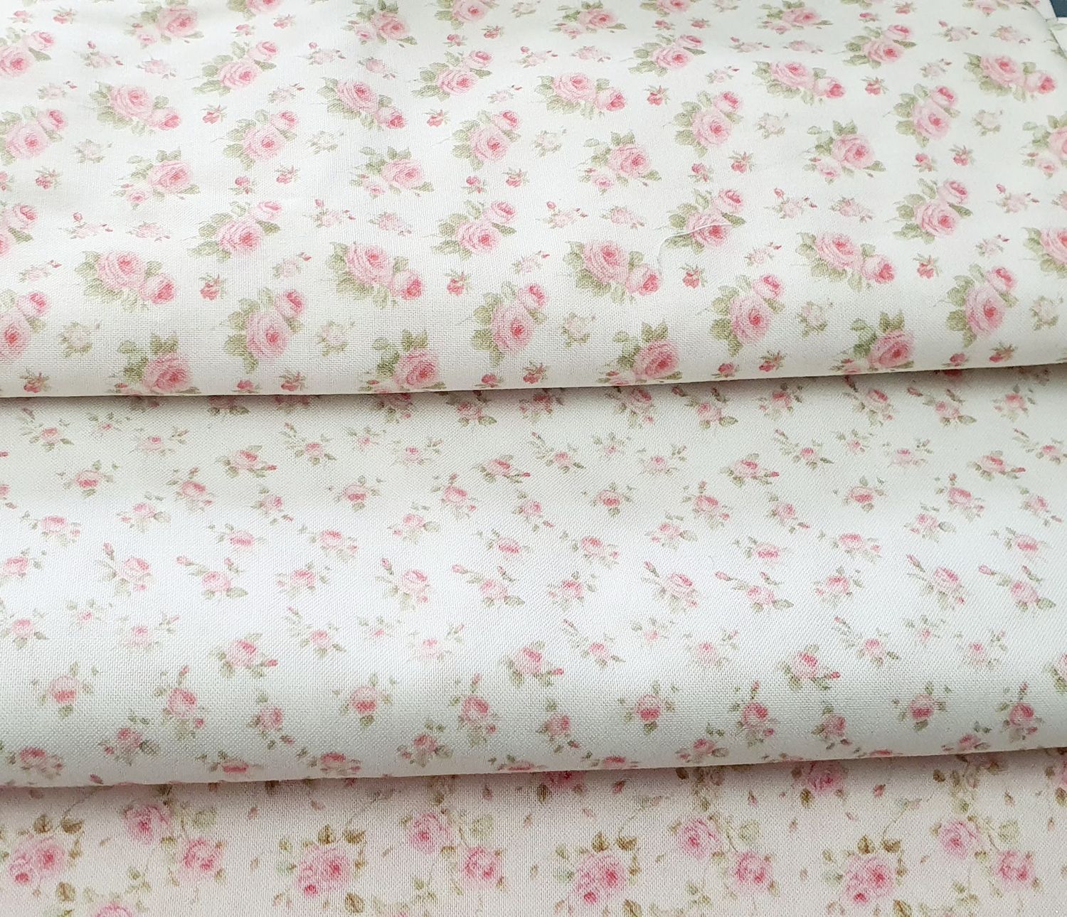 Delicate pink floral pattern fabric with small roses and green leaves on white cotton background.