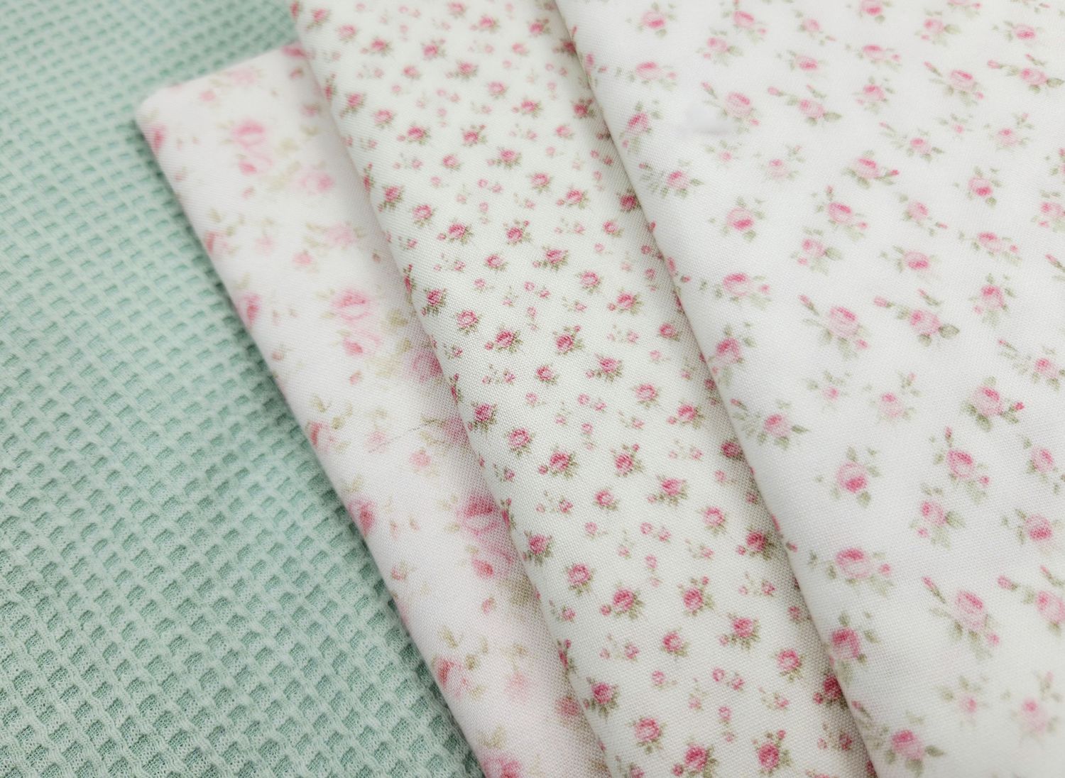 Folded white fabric with delicate pink floral pattern displayed on mint green textured surface.
