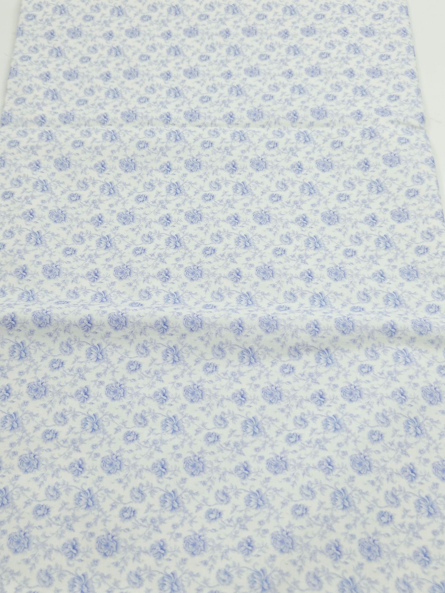 White fabric with delicate blue floral pattern in a repeating vintage style design.