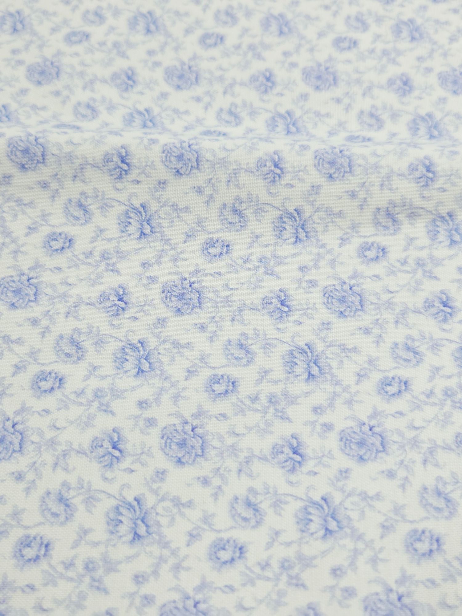 Delicate blue floral pattern on white fabric creates a soft vintage-inspired textile design.