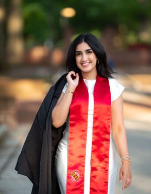 Graduate wearing red stole and black graduation gown poses outdoors.