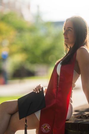 Graduate in red stole and black gown poses outdoors during sunset photo session.