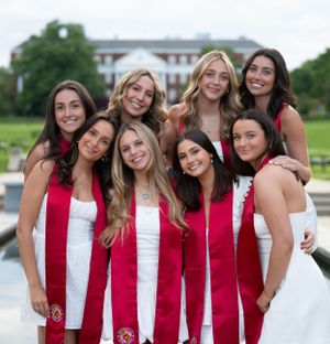 Group of graduates in red and white stoles pose together for celebration photo.