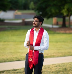 Graduate in cap and gown poses against green background during graduation photoshoot.