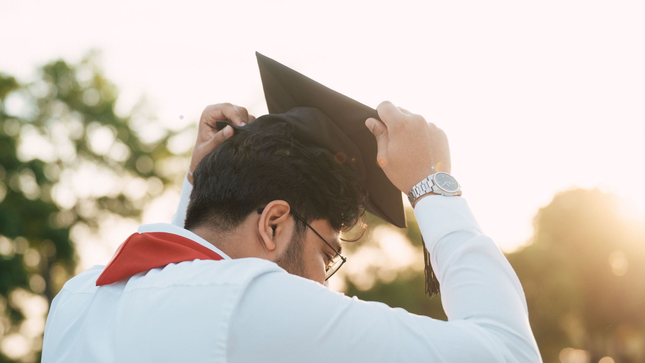 Graduates celebrating at sunset with graduation caps raised in the air.