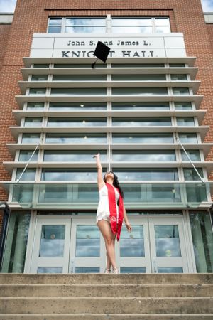 Graduate poses on concrete steps outside Knight Hall building.