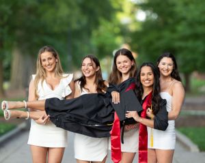 Graduates in white tops celebrate together outdoors during photo session.