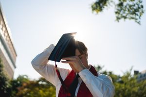 Graduation photoshoot with academic regalia against bright sky background.