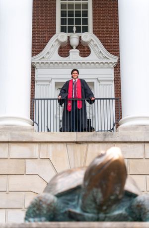 Graduate posing on balcony of brick building with white columns and ornate architecture.
