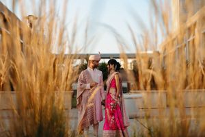 Couple in traditional Indian wedding attire photographed among tall wheat stalks at sunset.