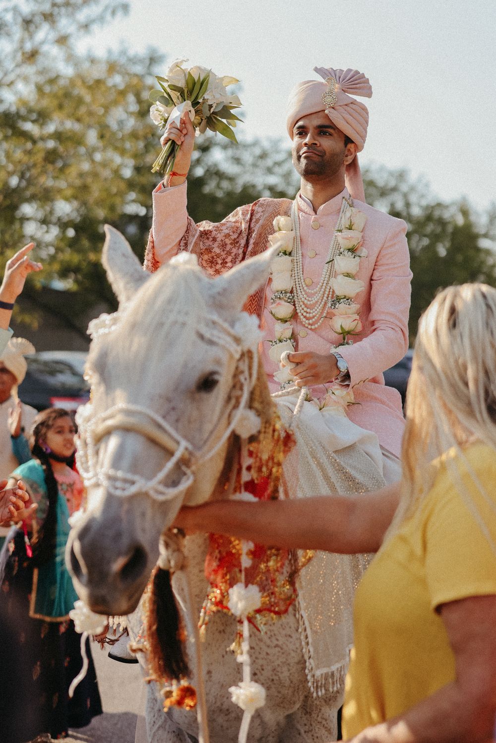 Traditional Indian baraat ceremony with decorated white horse and celebratory crowd gathering outdoors.