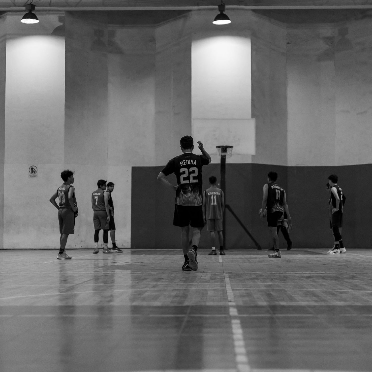 Black and white view of a spacious indoor gymnasium with scattered groups practicing.