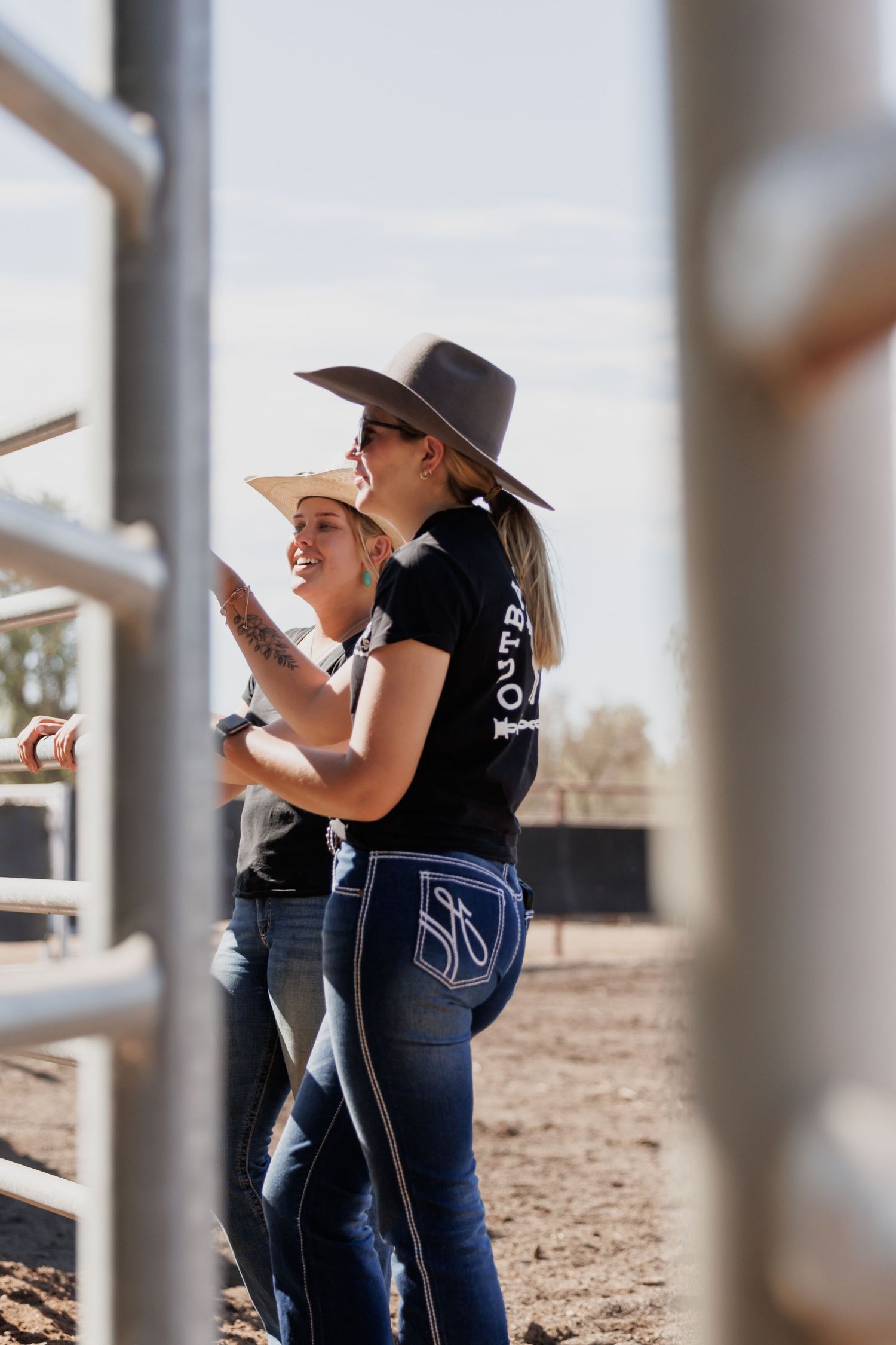 Two spectators in cowboy hats watching through arena fence rails.