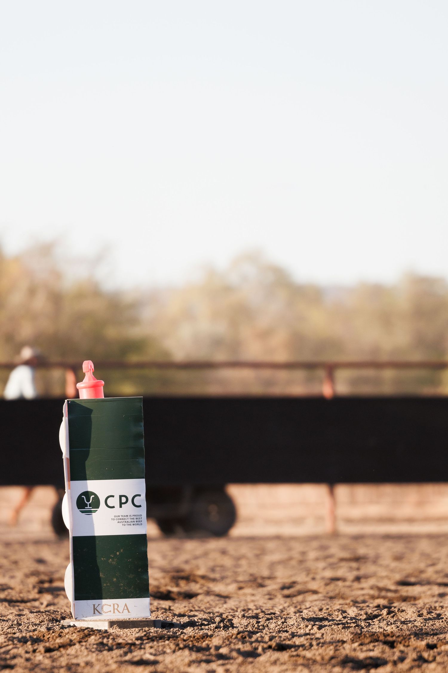 Green water bottle with CPC logo sitting on dirt ground at outdoor event.