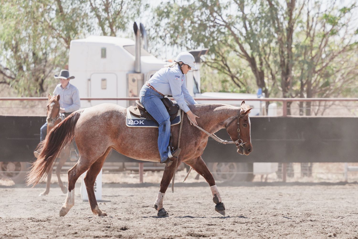 Western horse riders practicing in a dusty arena with wooden fencing.