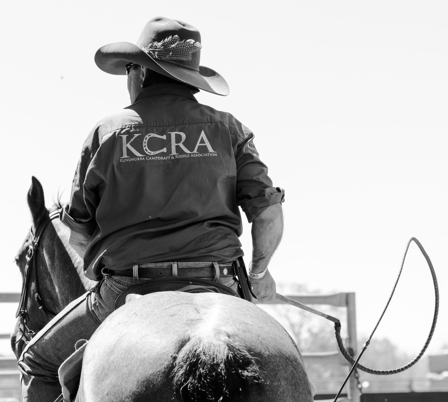 Rear view of KCRA official on horseback with lasso at rodeo event.