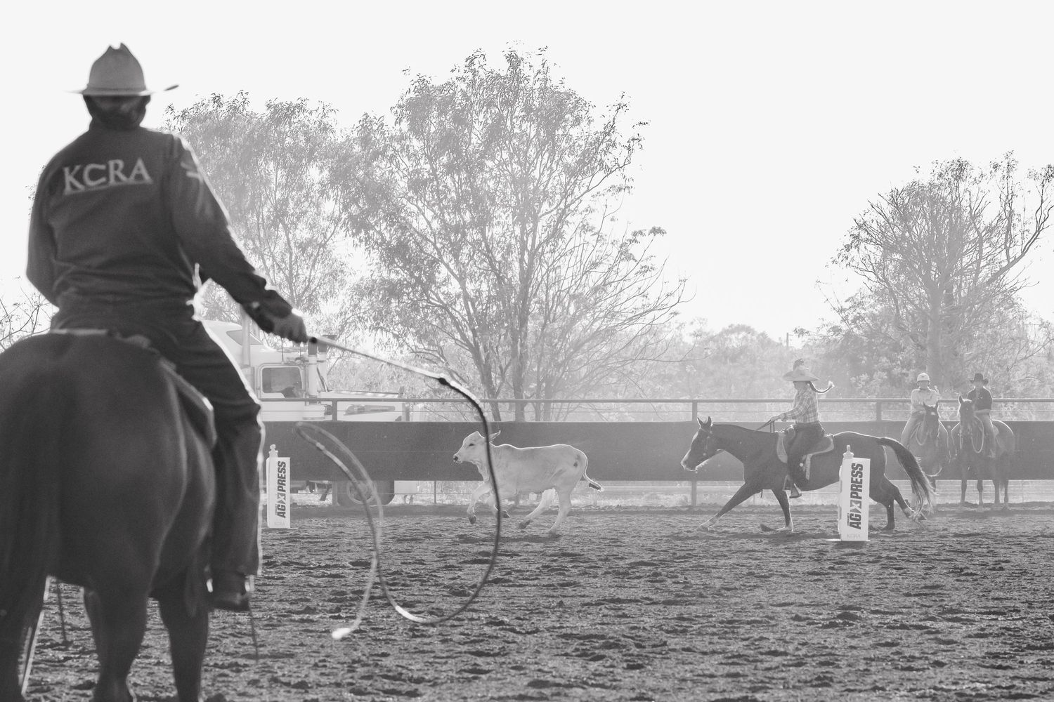 Cowboys practicing roping techniques on horseback in a dusty arena.