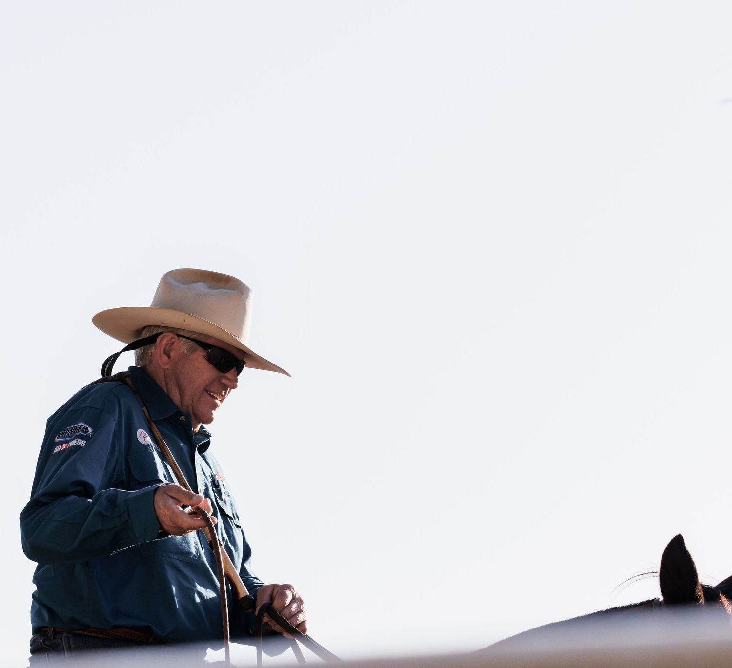A rider wearing a cowboy hat and denim jacket sits mounted on horseback.