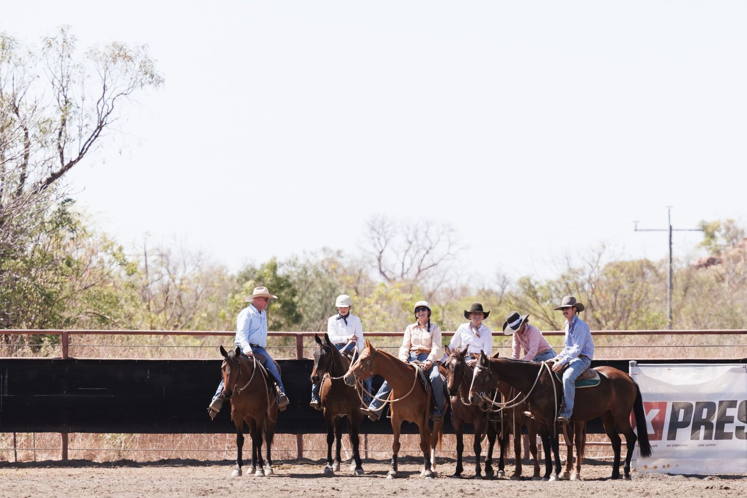 Five cowboys on horseback line up against a dark fence during a western riding event.