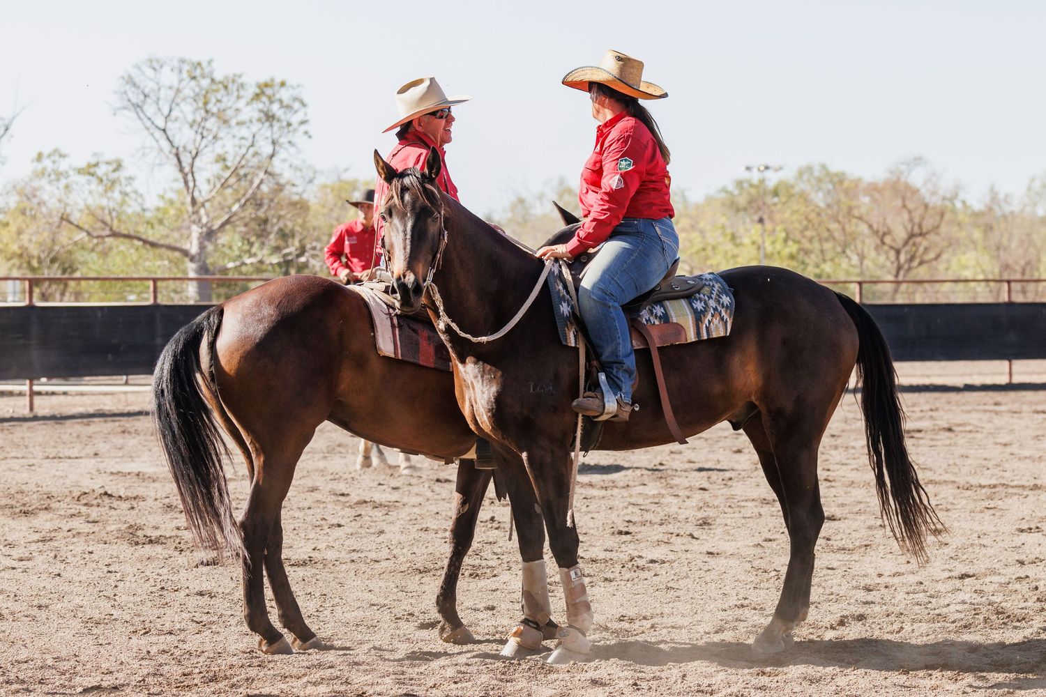 Two riders in red shirts stop their horses to chat during a western riding event.