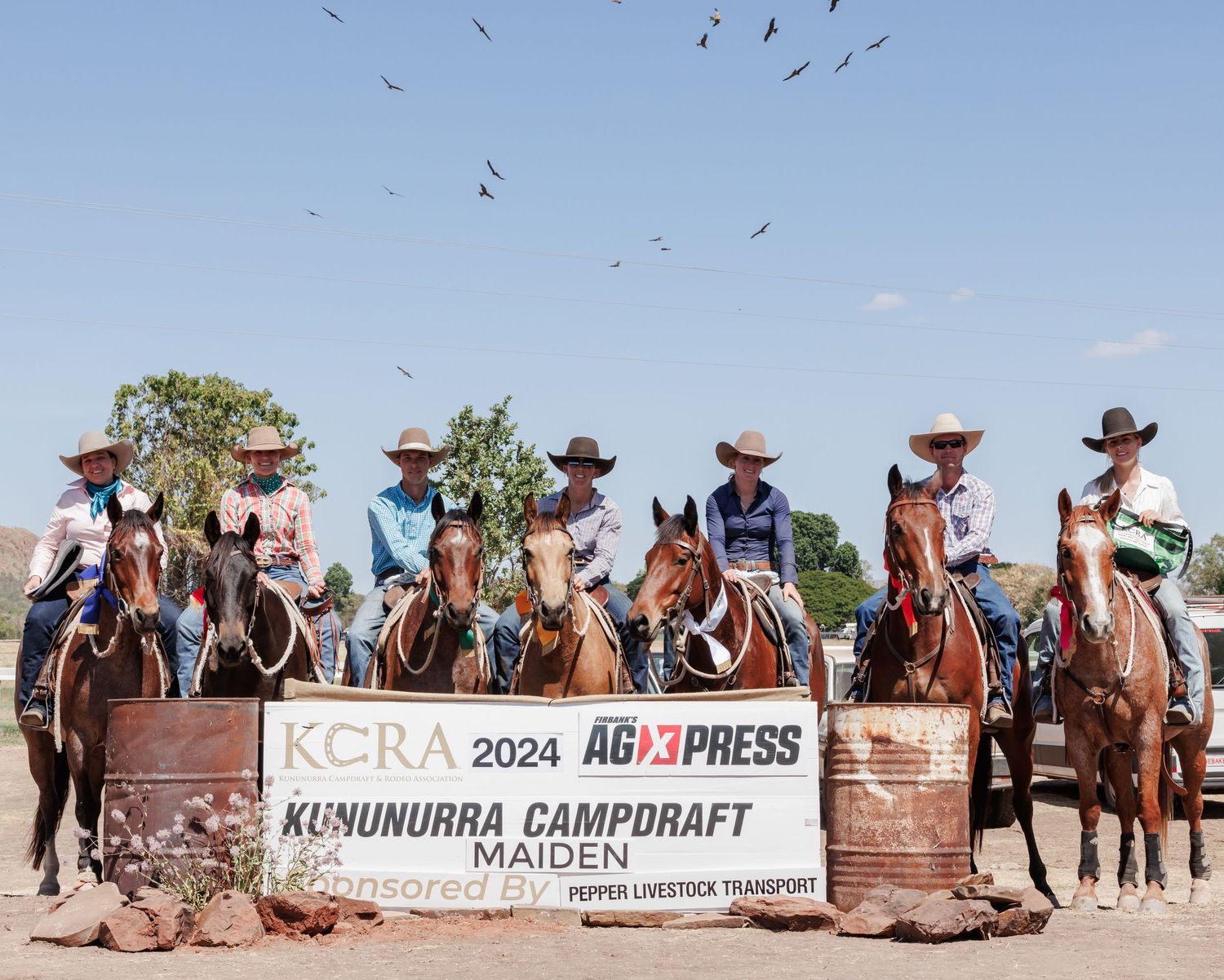 Group of riders on horseback lined up at KCRA campdraft event with birds flying overhead.