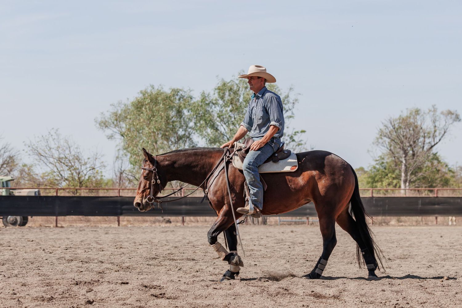 Rider guides horse through practice routine in dusty outdoor arena with wooden fence.