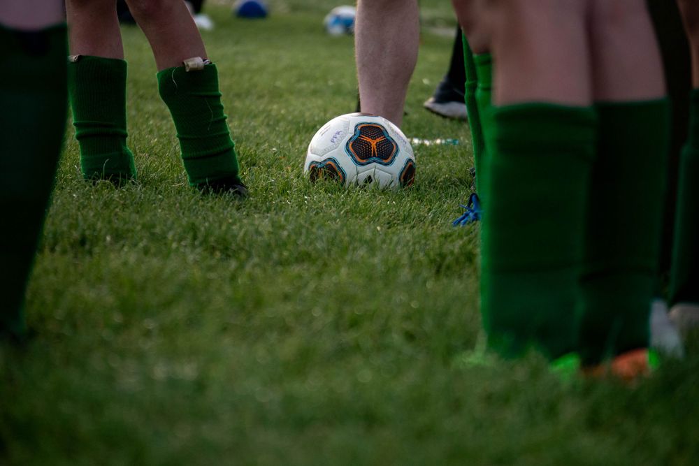 Soccer ball on grass field surrounded by players wearing green socks.