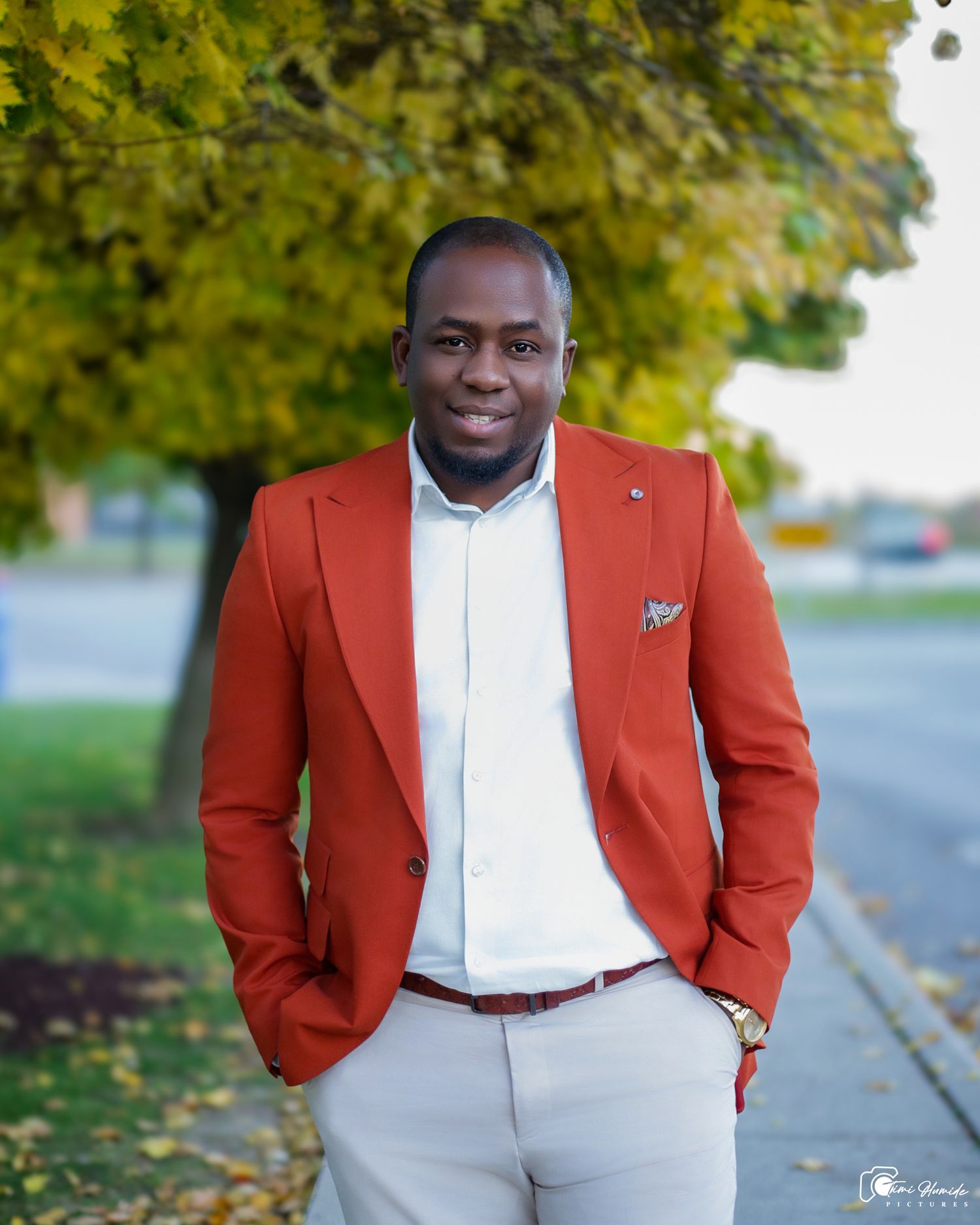 Professional portrait of someone in a stylish red blazer and white shirt against autumn foliage background.