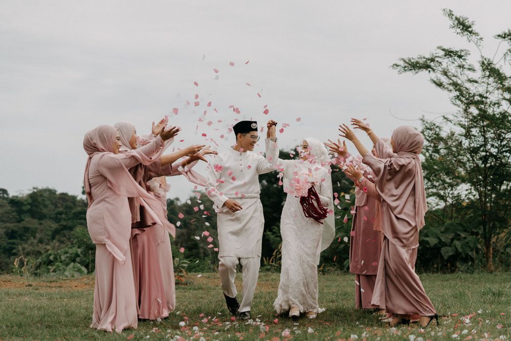 Joyful Malay wedding moment as the bride and groom walk through a shower of flower petals, surrounded by bridesmaids. Hizashi Studio