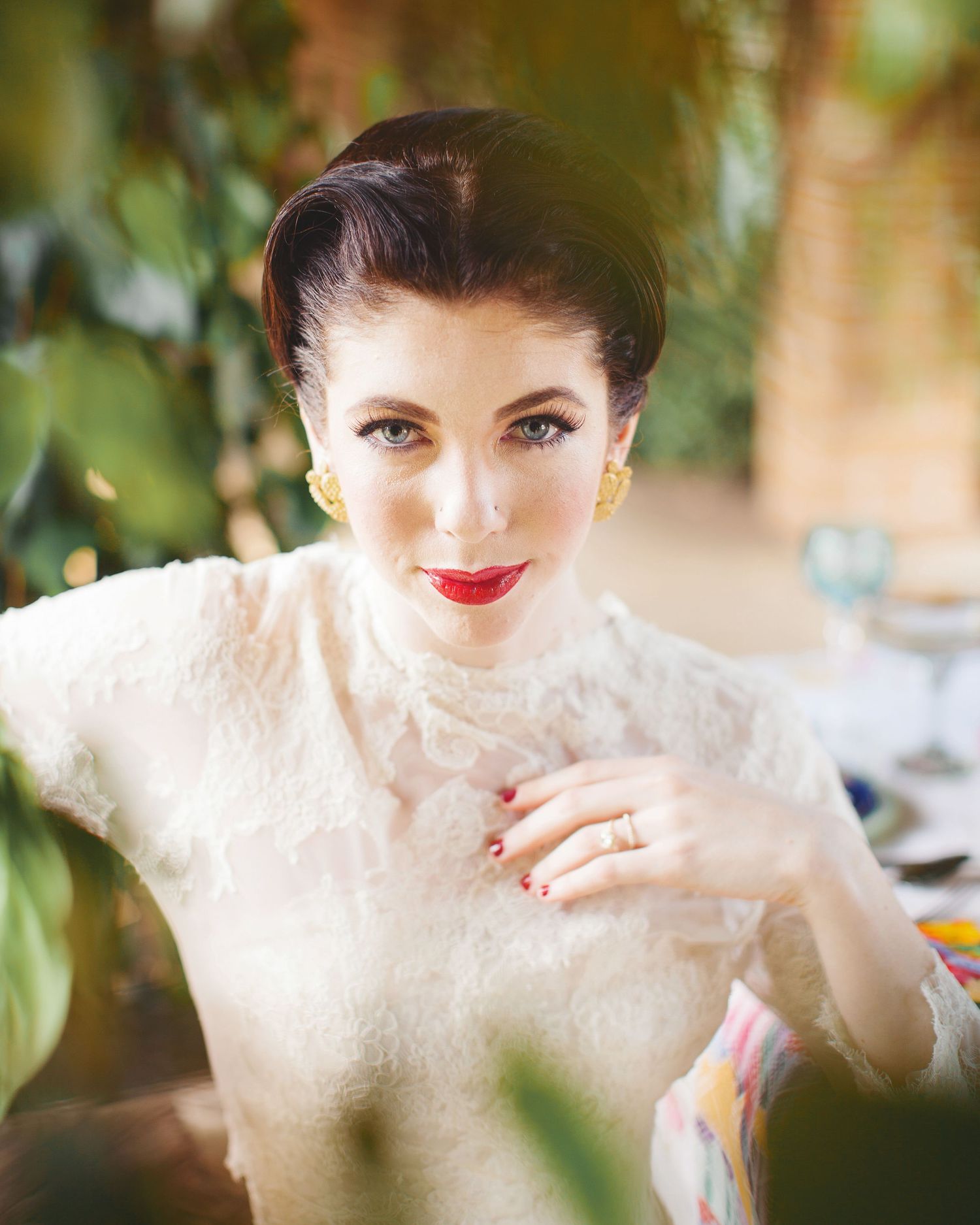 Woman in vintage lace dress with red lipstick poses in garden setting.