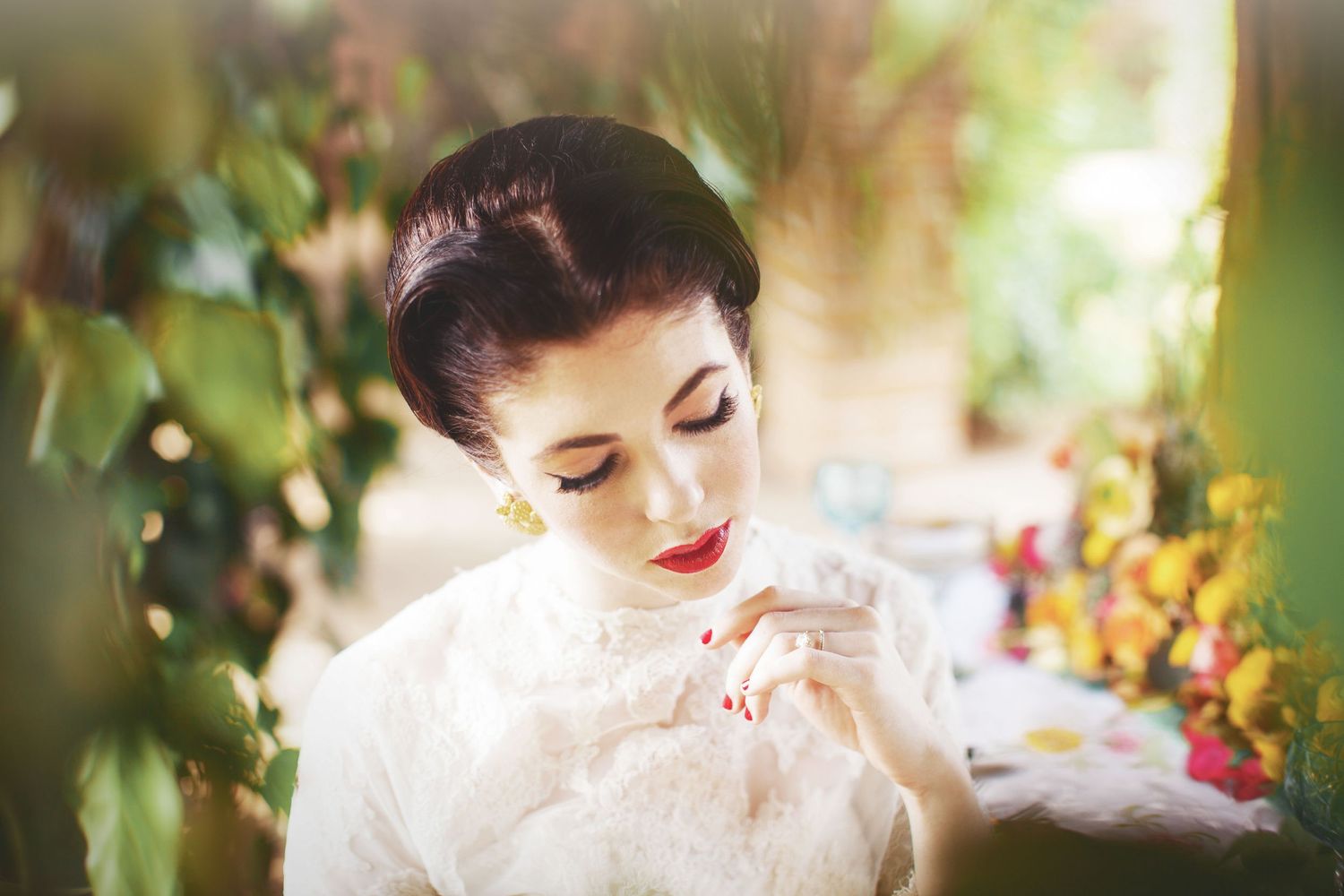 Portrait of woman in white lace dress gazing down with classic makeup.