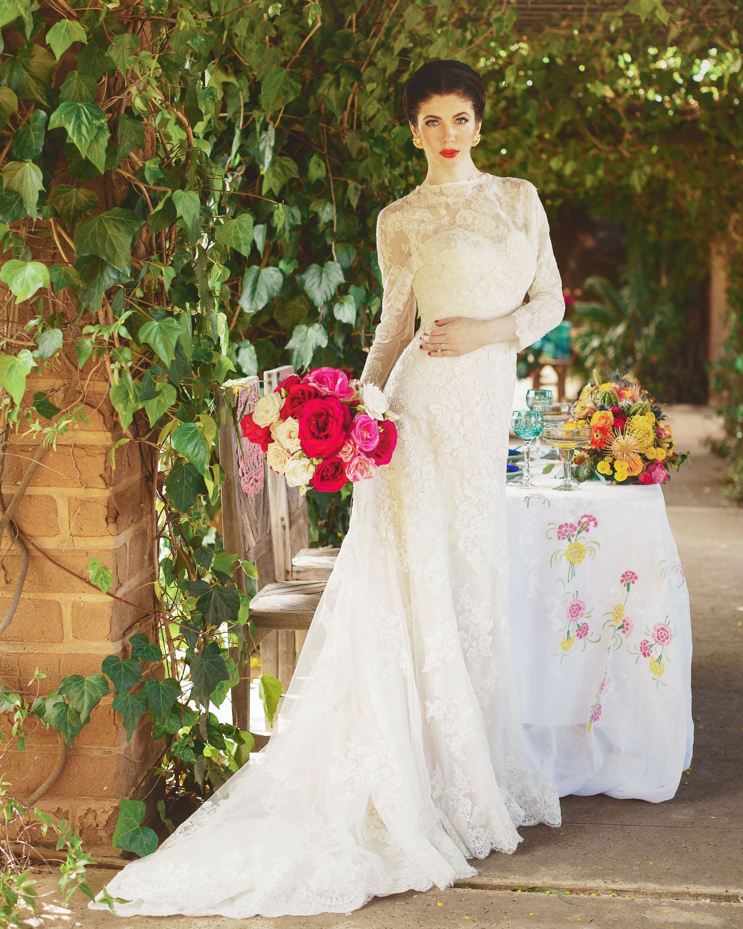 Elegant lace wedding dress with long sleeves and train photographed in a garden setting with bright pink floral bouquet.