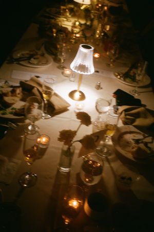 An illuminated small table lamp creates ambiance on a dinner table with glassware and candlelight.