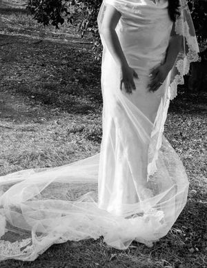A flowing white wedding dress train with delicate tulle fabric trails across grass in an outdoor setting.