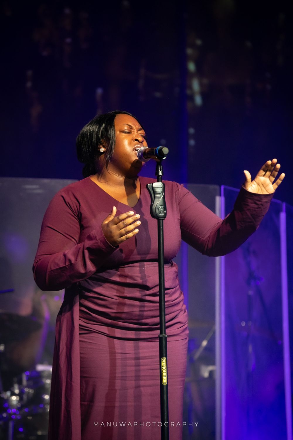 Singer performing passionately on stage in purple dress with microphone.