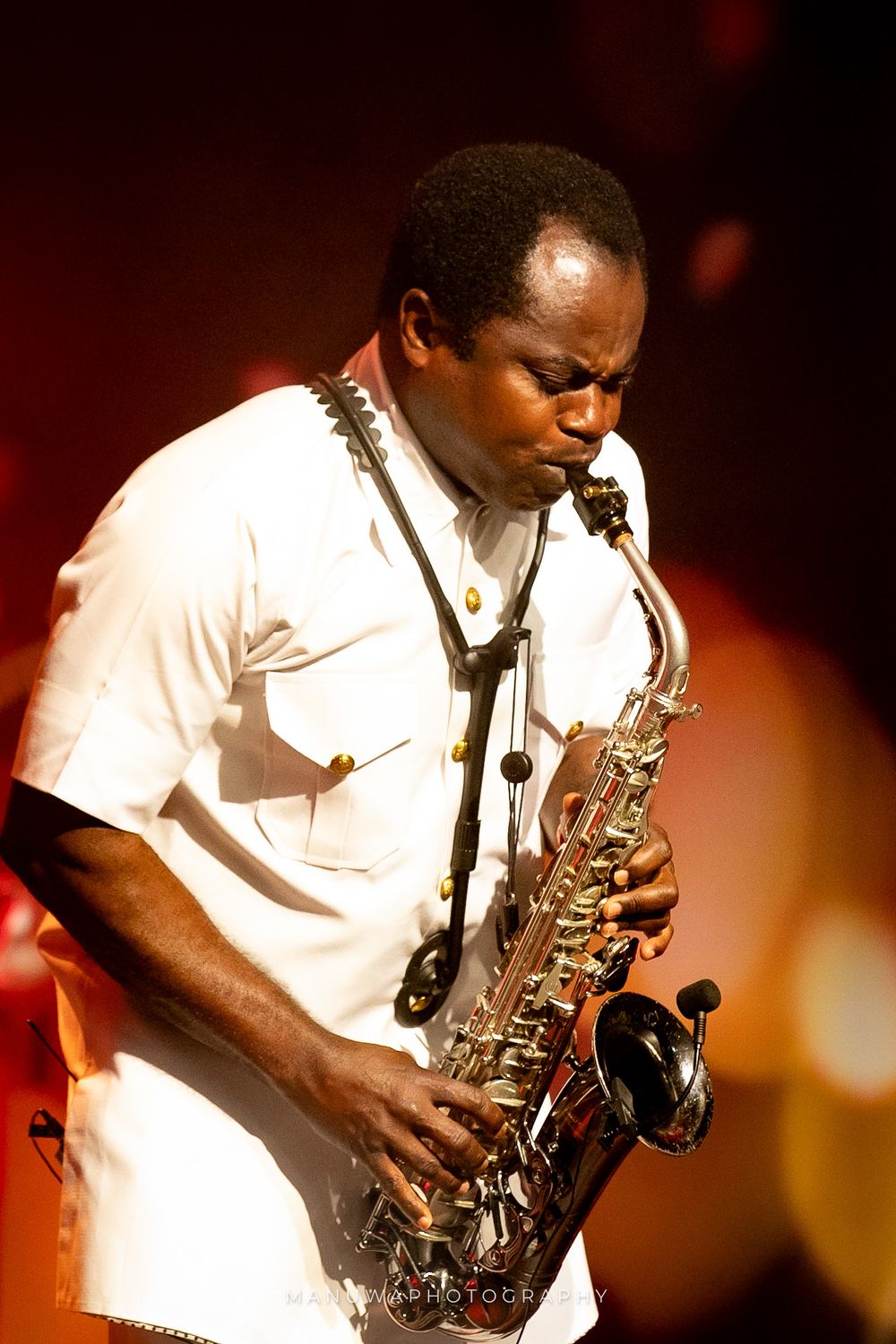 Saxophone player in white shirt performs passionately against warm-toned stage lighting.