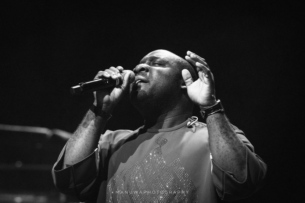 Black and white concert photo of performer singing passionately into microphone.
