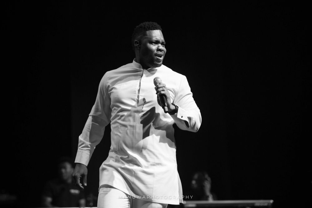 Performer in white outfit singing on stage in dramatic black and white.