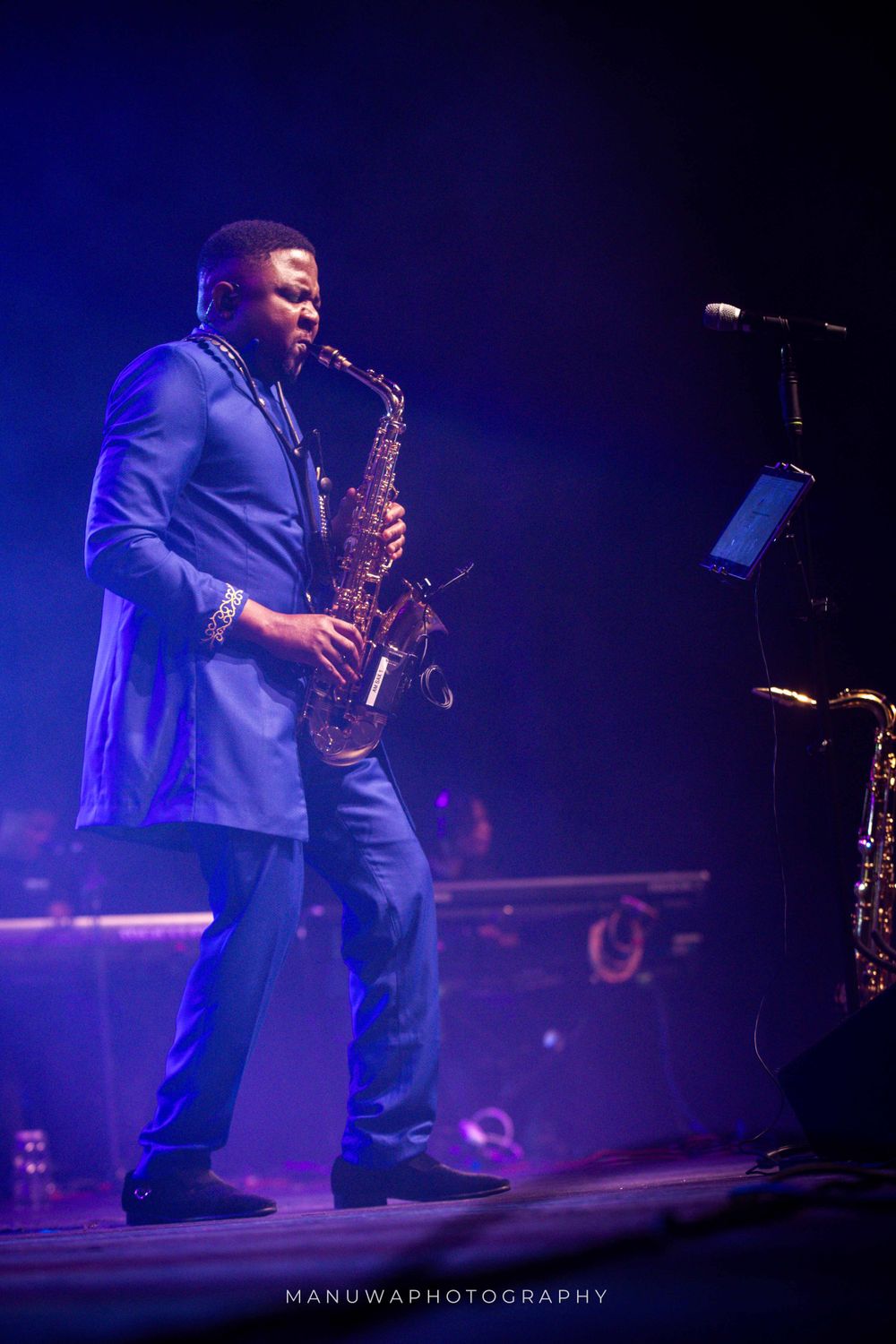 Saxophonist performing under blue stage lights in elegant blue suit.