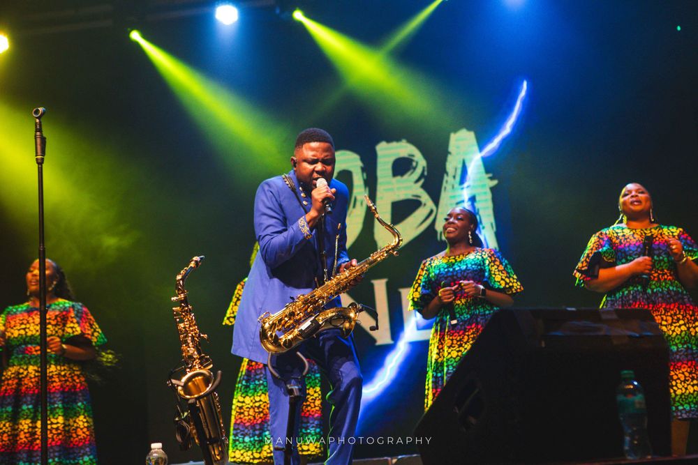 Vibrant concert performance with colorful lighting and performers in traditional African print dresses.