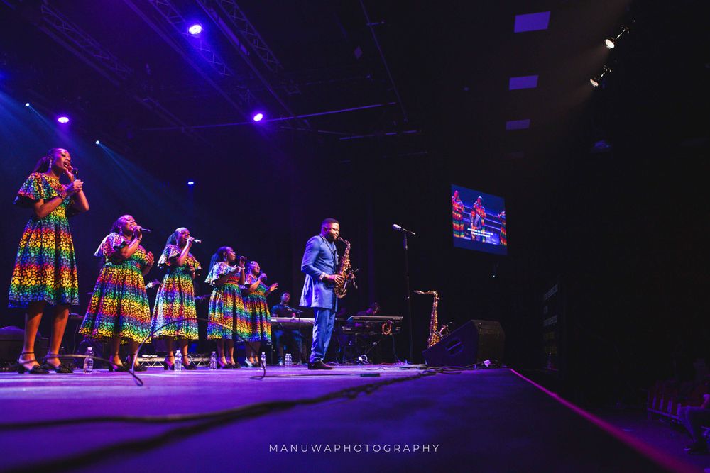 Wide stage shot of musical ensemble with bright lighting and traditional African costumes.
