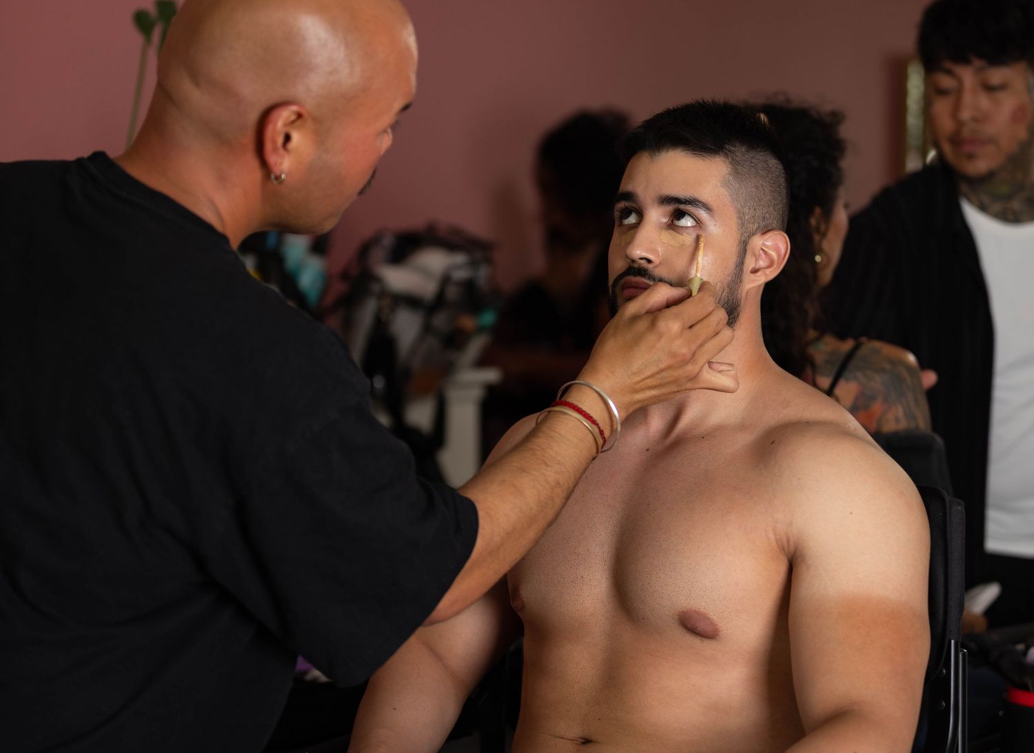 Hair and makeup artist preparing male client for a boudoir photo shoot.