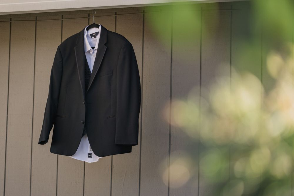 A formal black suit jacket and white dress shirt hanging on display against a beige wall.