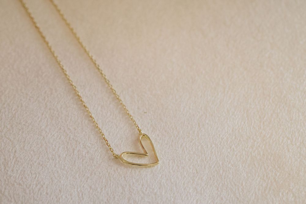 Delicate gold heart pendant necklace displayed on soft beige background.