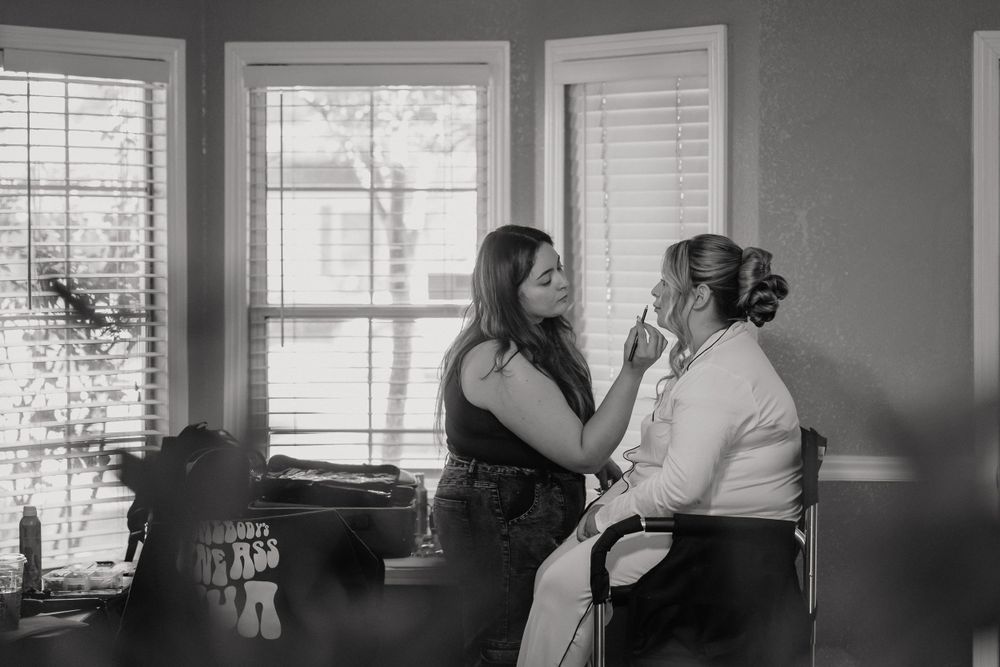 Professional makeup artists prepare a bride for her wedding day in a sunlit room.