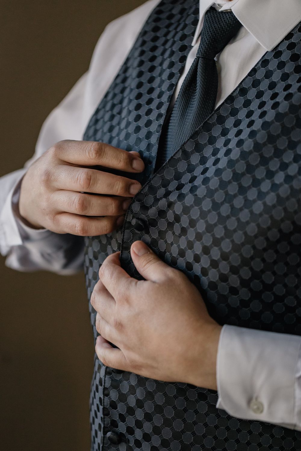 Close-up of hands adjusting a polka dot vest with dark tie and white dress shirt.