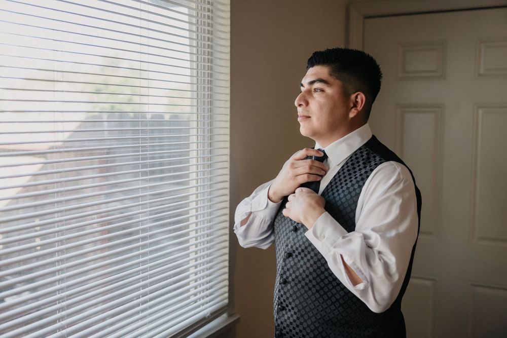 A well-dressed figure standing by a window in formal attire with patterned vest.